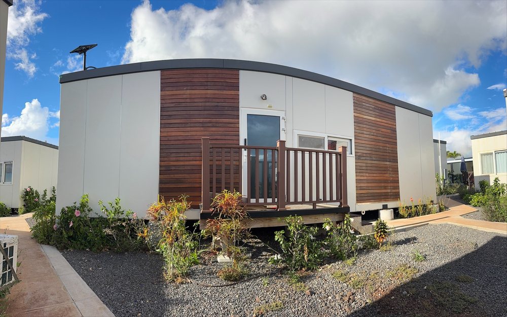 A single-story modular home with wood siding, a small front deck and landscaping.